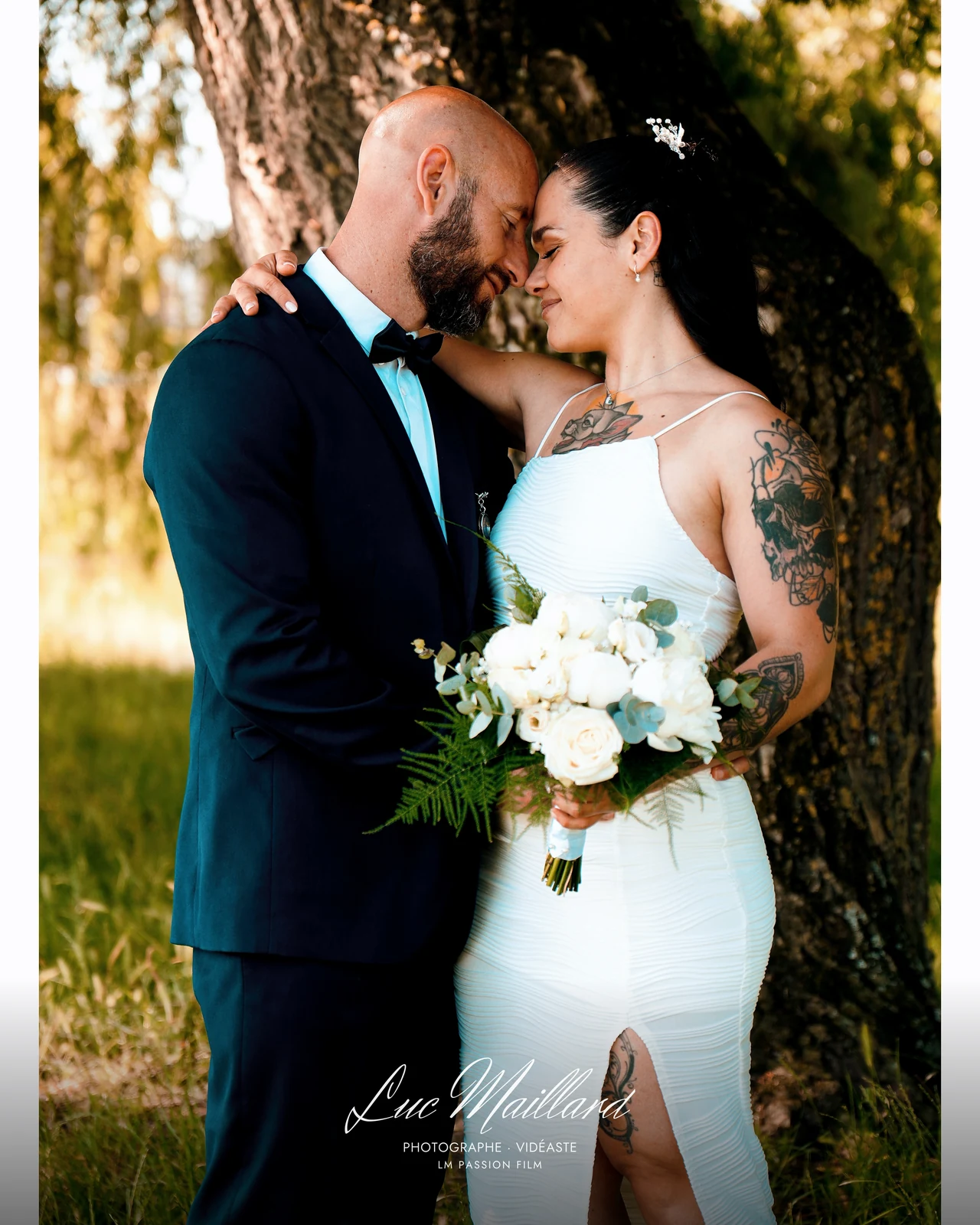 Couple de mariés front contre front sous un arbre