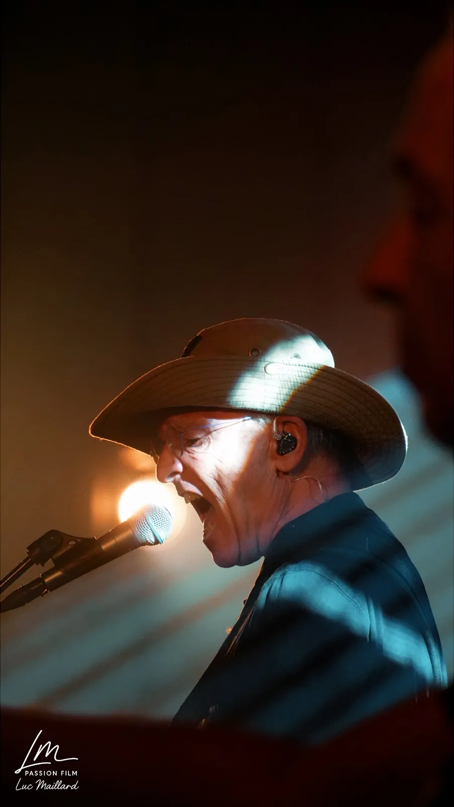 Chanteur au chapeau au micro, lumière chaude en contre-jour